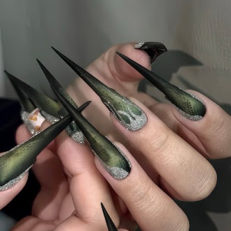 Long deep green stiletto press-on nails with a mottled texture and silver glitter at the base, worn on a hand