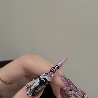 Long pointed translucent pink nails with black artwork and silver metallic charms, worn on a hand