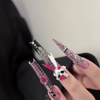 Long pink and black nails with rhinestone lines and a black-and-white bow accent, worn on a hand