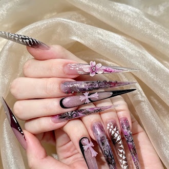 Long translucent pink stiletto nails with dark lace patterns, raised pink flowers, and bows, worn on two hands